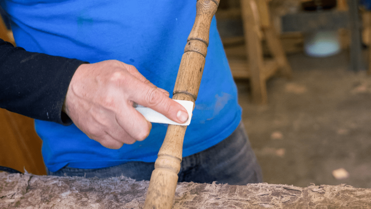 A hand sanding down a wooden dowel